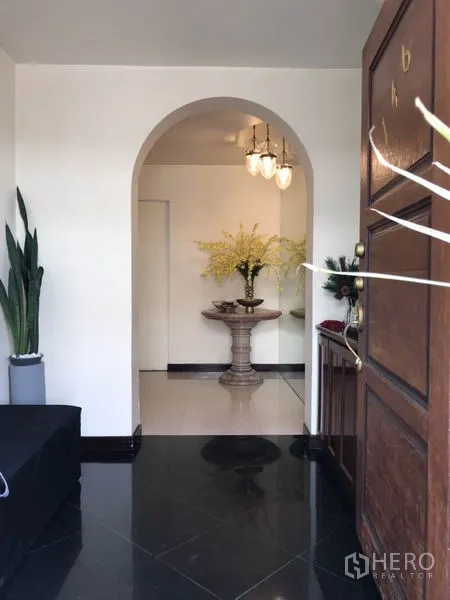 Detached House for rent in Phra Khanong, Bangkok - Wooden front door opening to an arched hallway with decorative flowers and lighting.