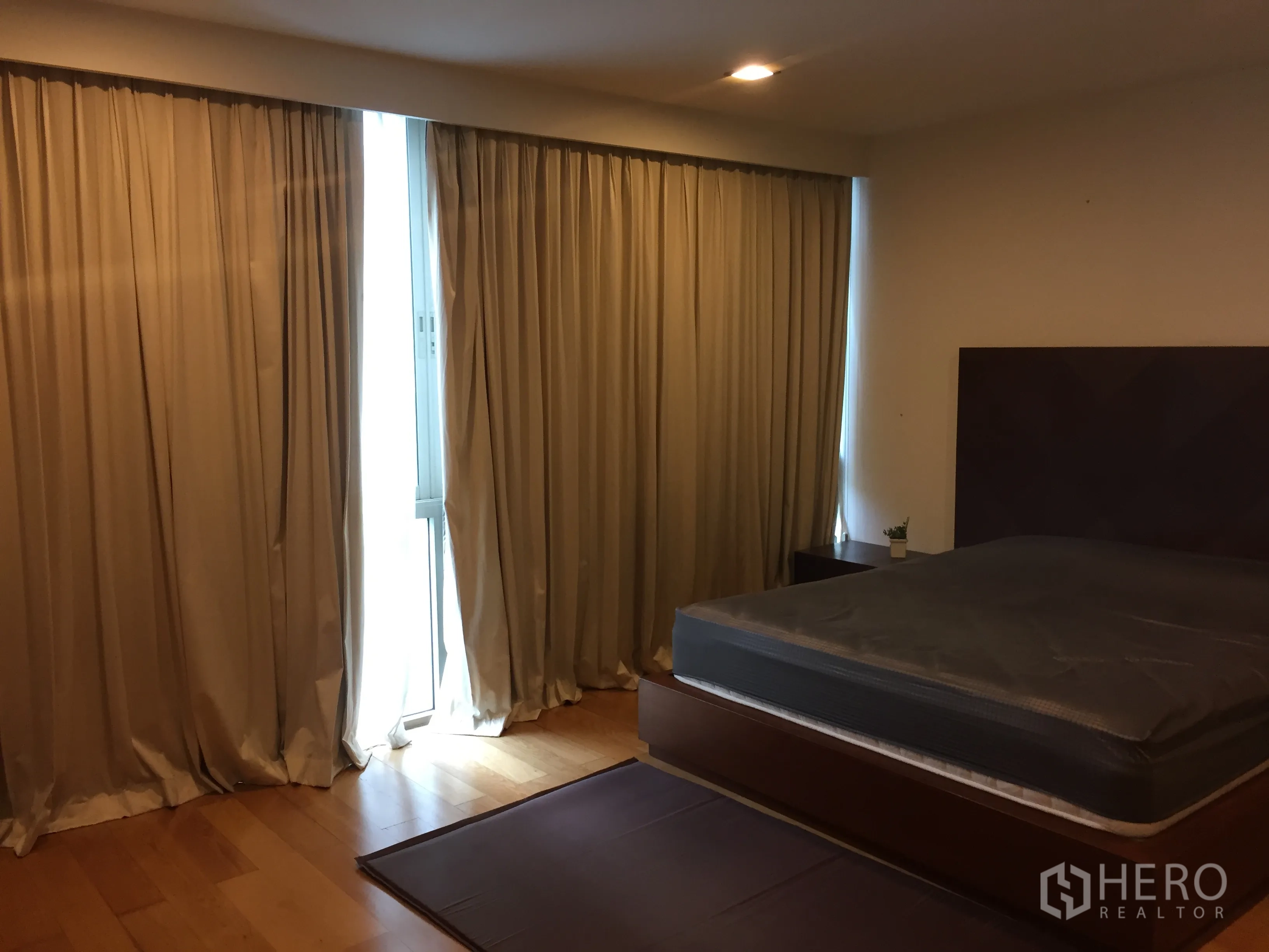 Condominium for rent in Khlong Toei, Bangkok - Spacious bedroom with floor-to-ceiling curtains, wood flooring, and a large bed.
