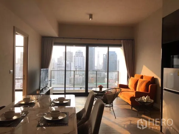 คอนโด ขายในWatthana, Bangkok - ห้องนั่งเล่นและรับประทานอาหารสว่างไสว พร้อมโต๊ะหินอ่อน โซฟาสีส้ม และกระจกเต็มผนังเปิดสู่ระเบียงชมวิวสกายไลน์กรุงเทพฯ