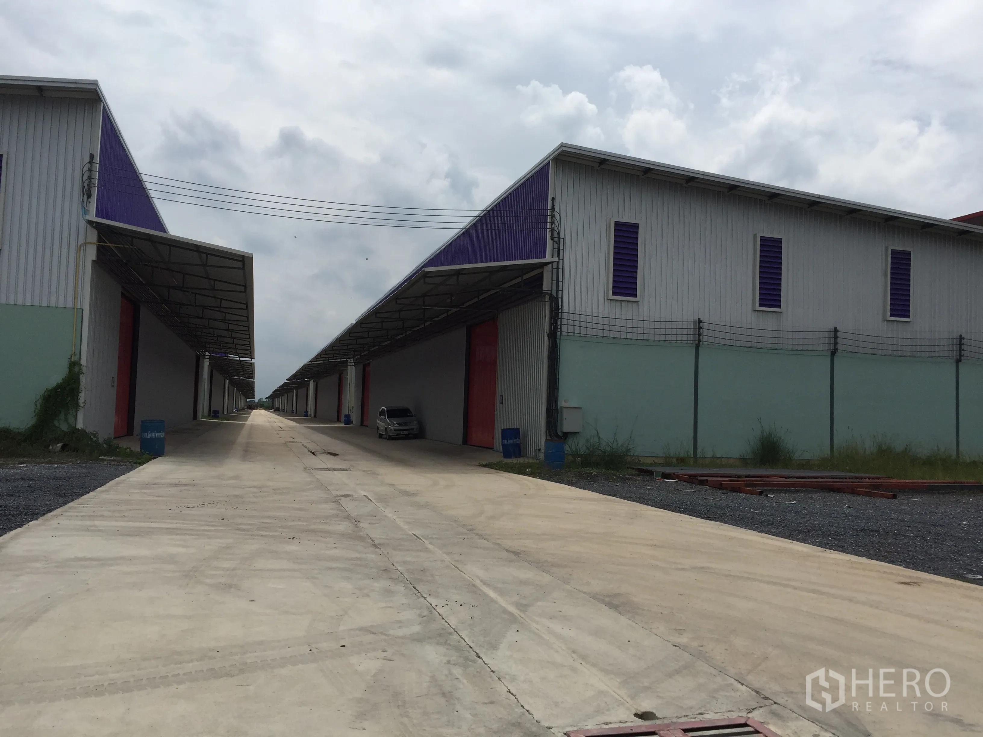 Warehouse for rent in Pathum Thani - Twin warehouse blocks facing a central concrete road with canopies and red loading doors.