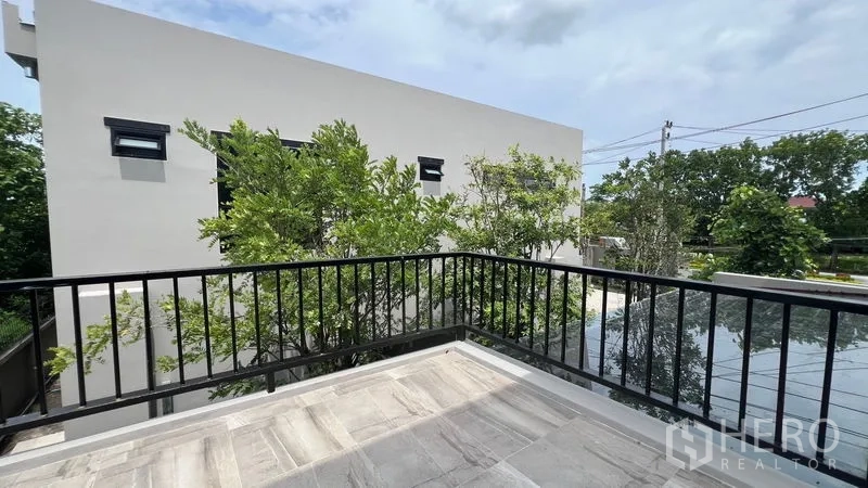 独立式住宅 出租在Lat Krabang, Bangkok - 二层阳台黑色栏杆，俯瞰绿树与邻近现代住宅。