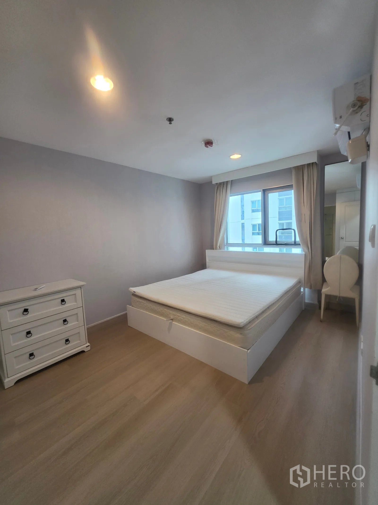 Condominium for rent in Huai Khwang, Bangkok - Sunlit bedroom with bed, dresser, and a chair by the window.