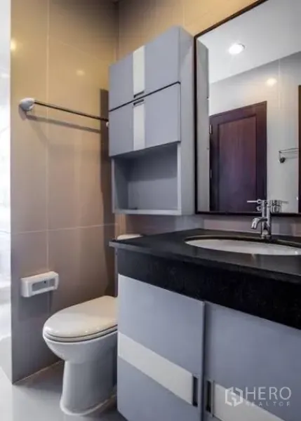 Condominium for rent or sale in Watthana, Bangkok - Modern bathroom with vanity, mirror, wall cabinets and toilet.