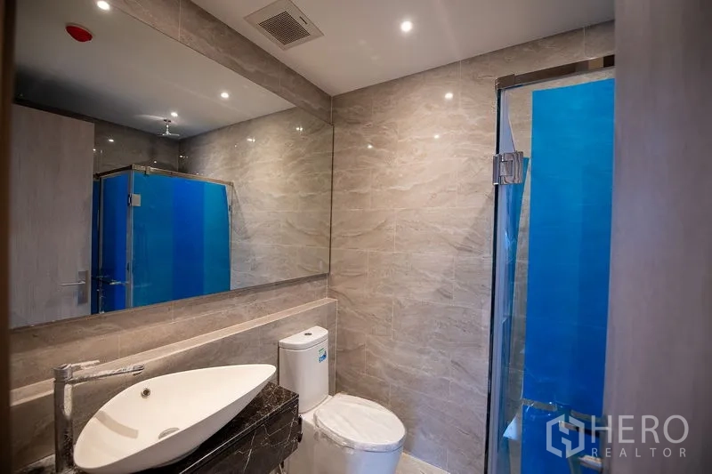 Condominium for rent in Din Daeng, Bangkok - Modern bathroom with marble-look tiles, vessel sink, toilet and a glass shower enclosure.