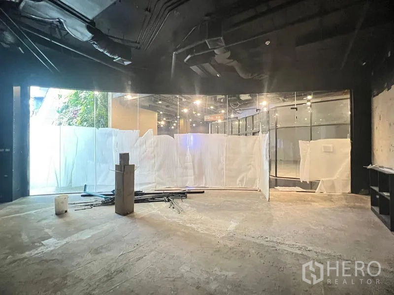 Retail Space for rent - Empty 50 sqm retail unit with high exposed ceiling, spot lighting, and a curved floor-to-ceiling glass shopfront under preparation.