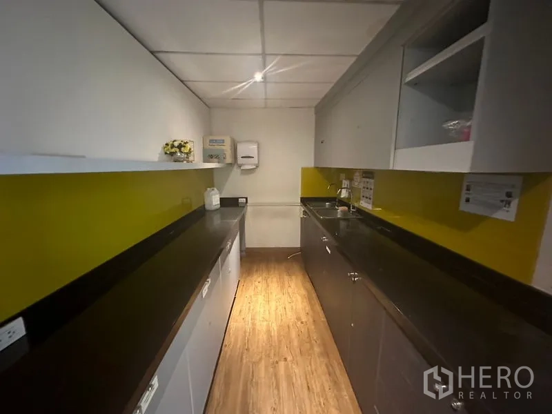 Office Space for rent in Khlong Toei, Bangkok - Galley pantry with long black countertops, sink, and a yellow backsplash inside the office.