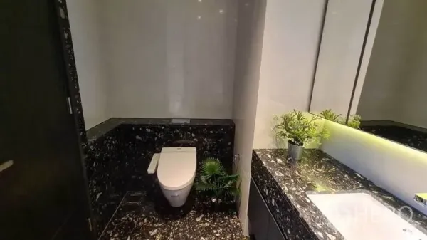 Condominium for rent in Khlong Toei, Bangkok - Modern bathroom with black marble vanity, large mirror and toilet in a Bangkok condo.