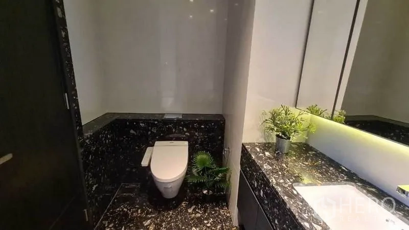 Condominium for rent in Khlong Toei, Bangkok - Modern bathroom with black marble vanity, large mirror and toilet in a Bangkok condo.