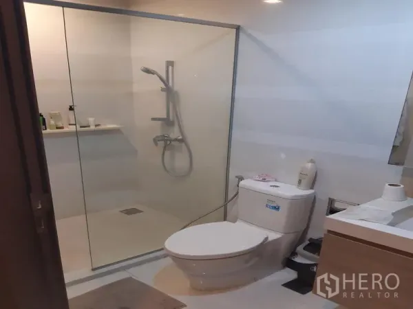 Condominium for rent or sale in Khlong Toei, Bangkok - Contemporary bathroom with glass-enclosed shower, handheld shower set, vanity and tiled walls.