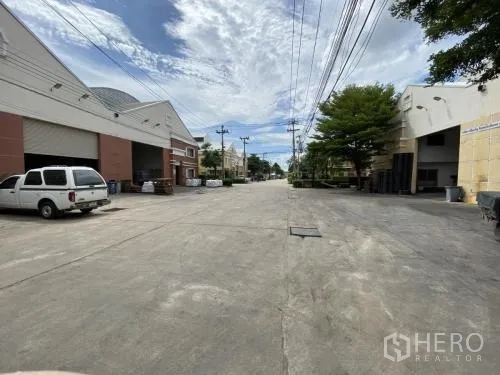 Warehouse for rent in Samut Sakhon - Wide concrete street with warehouses on both sides and overhead utilities.