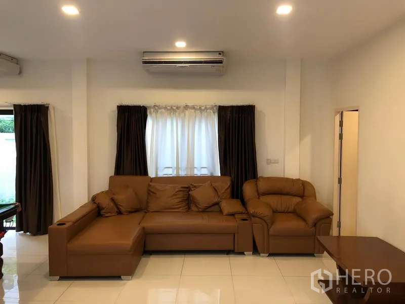 ทาวน์เฮาส์ ให้เช่าหรือขายในSaphan Sung, Bangkok - ห้องนั่งเล่นอบอุ่น โซฟาหนังสีน้ำตาล ผ้าม่าน และเครื่องปรับอากาศติดผนัง