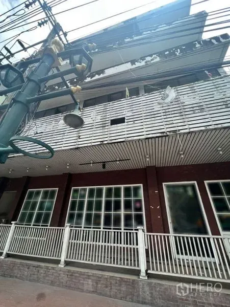 Shophouse for rent in Watthana, Bangkok - Multi-storey shophouse exterior with balcony, large shopfront windows and street power lines.