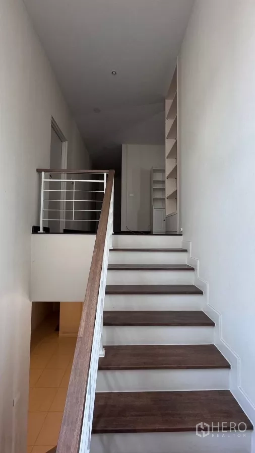 Detached House for rent or sale in Saphan Sung, Bangkok - Staircase with wood steps and white handrail ascending to an upper landing with open shelving.
