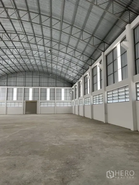 工厂 出租或出售在Bang Bo, Samut Prakan - 明亮的厂房内部长视角，成排窗户与弧形钢桁架屋顶。