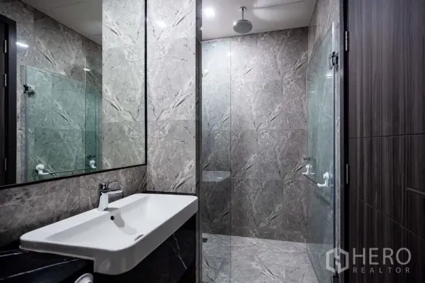Condominium for rent in Watthana, Bangkok - Modern bathroom with marble walls, glass shower enclosure and rain shower.