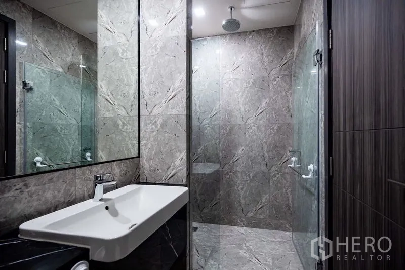 Condominium for rent in Watthana, Bangkok - Modern bathroom with marble walls, glass shower enclosure and rain shower.