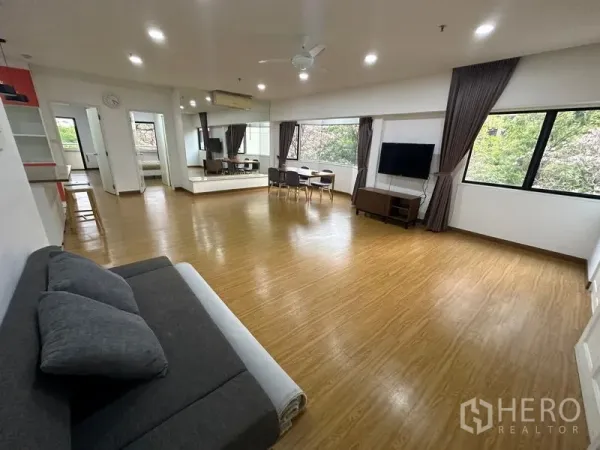 Condominium for rent in Watthana, Bangkok - Expansive living room with wood flooring, corner windows, TV and dining nook.