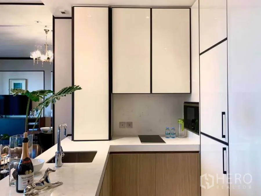 Condominium for rent in Khlong Toei, Bangkok - Sleek U-shaped kitchen with white cabinetry, stone countertops, built-in hob and ample storage.