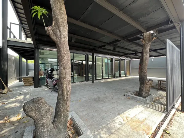 Detached House for rent or sale in Phra Khanong, Bangkok - Spacious covered carport with trees growing through openings and glass sliding doors to the home.