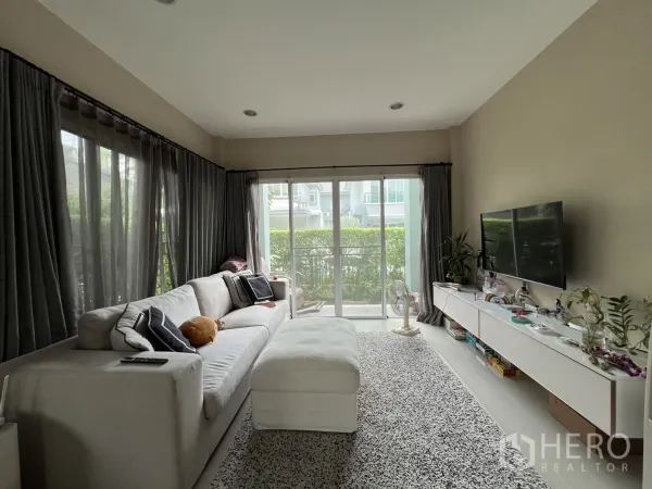 Detached House for rent or sale in Saphan Sung, Bangkok - Bright living room with large sofa, TV wall and floor-to-ceiling glass doors.