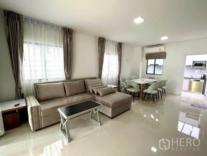 联排别墅 出租在Wang Thonglang, Bangkok - 客厅设L形沙发与餐桌，可通往独立厨房。