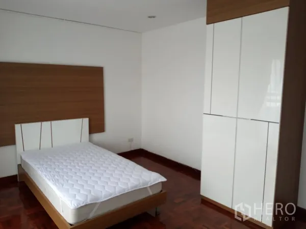 房间 出租在Watthana, Bangkok - 卧室配双人床、白色亮面衣柜与木质装饰墙。