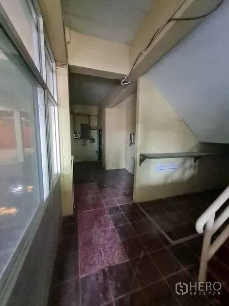 Warehouse for rent in Bang Yai, Nonthaburi - Interior corridor with staircase, utility panels and dark red tiled flooring.