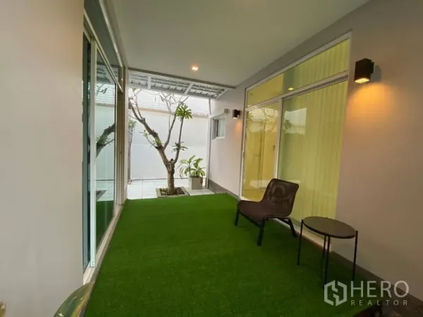 Detached House for rent or sale in Prawet, Bangkok - Covered patio with artificial grass, sliding glass doors and wall lights connecting to indoor living areas.
