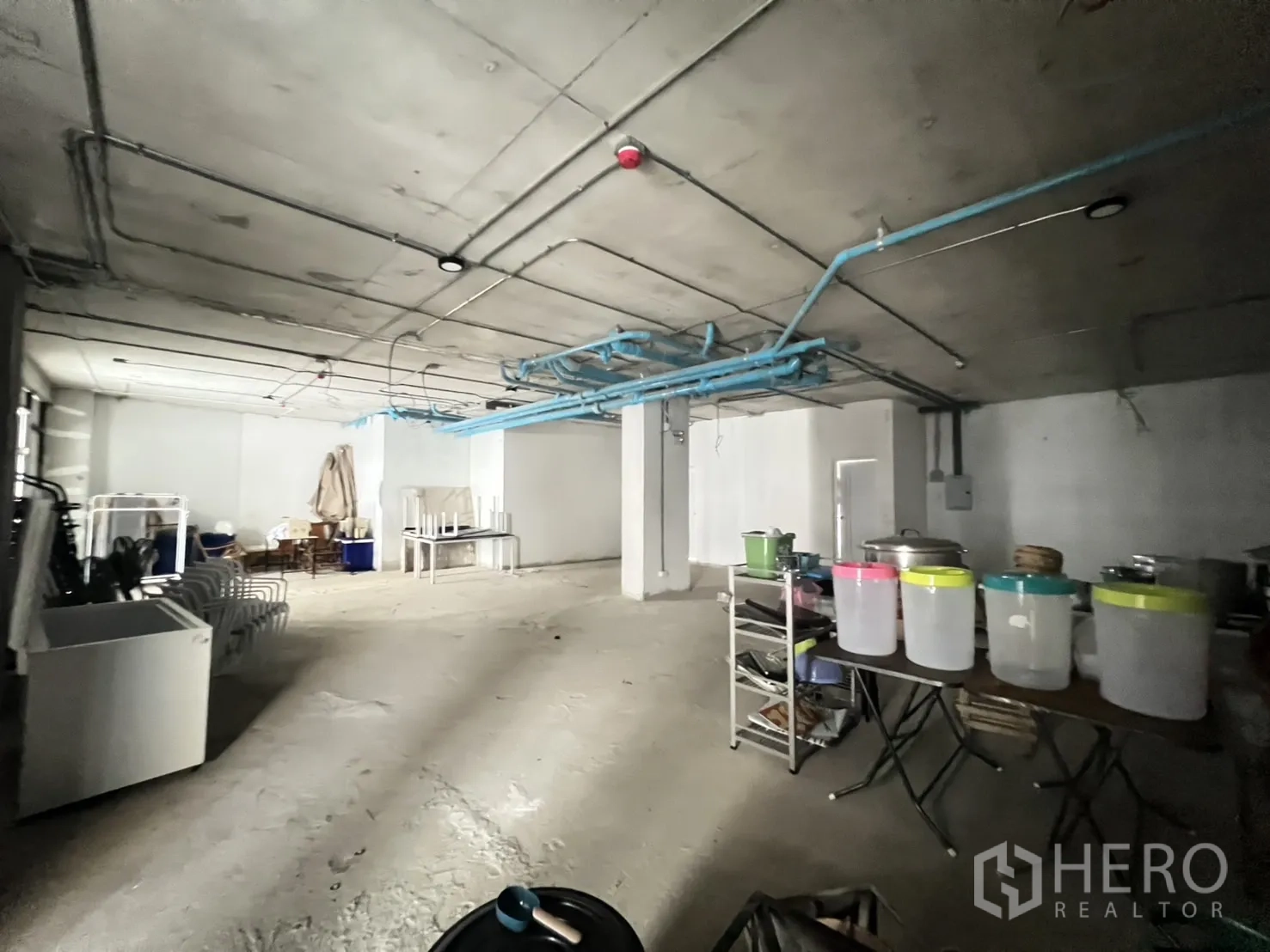 Retail Space for rent - Unfinished retail floor with equipment storage and stacked chairs near a windowed roller door.
