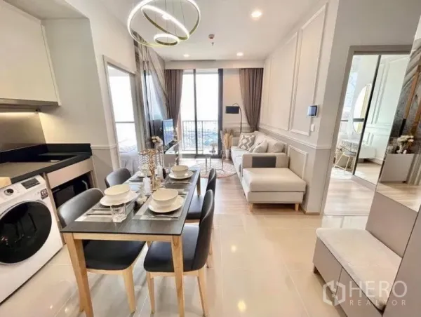Condominium for rent in Khlong Toei, Bangkok - Compact dining area beside a fitted kitchen with washing machine, leading toward the balcony and living zone.