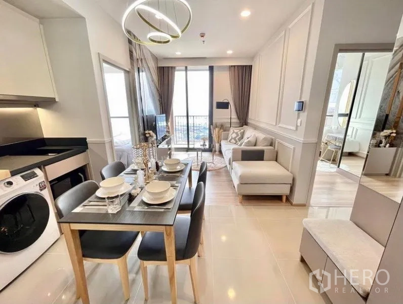 Condominium for rent in Khlong Toei, Bangkok - Compact dining area beside a fitted kitchen with washing machine, leading toward the balcony and living zone.