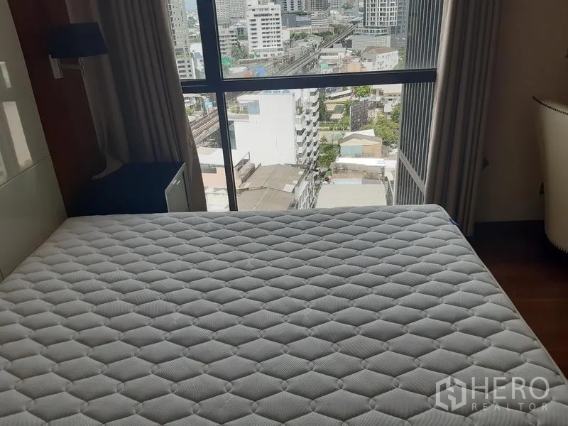 Condominium for rent in Khlong Toei, Bangkok - Bedroom with large window overlooking city streets and rail line.