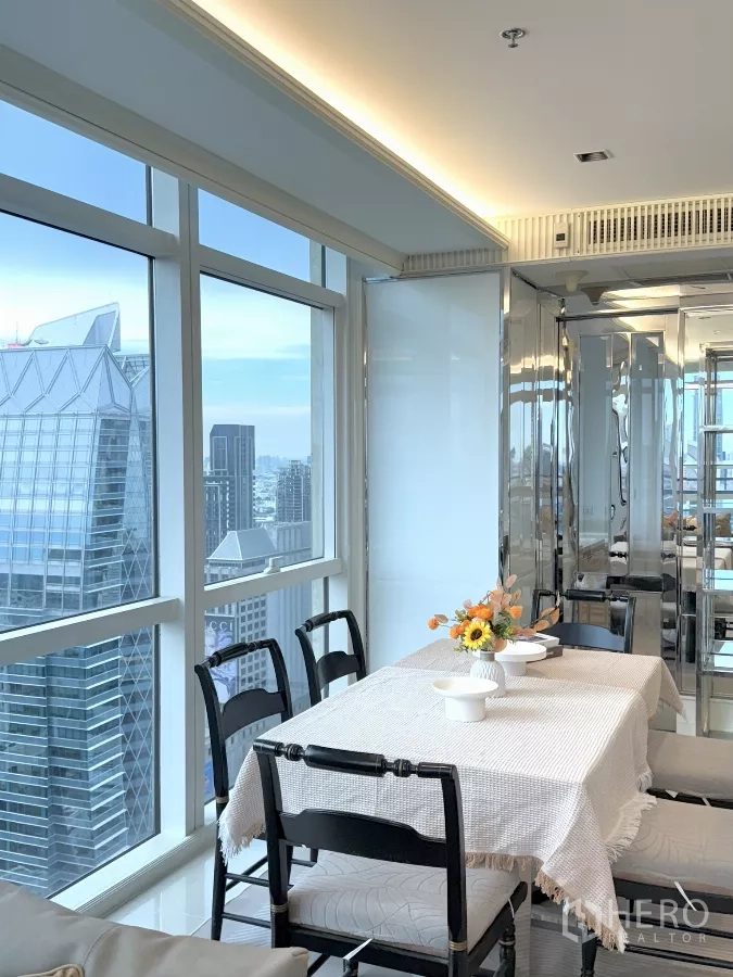 公寓 出租在Pathum Wan, Bangkok - 转角玻璃旁的餐区，镜面墙与城市高楼相映成景。