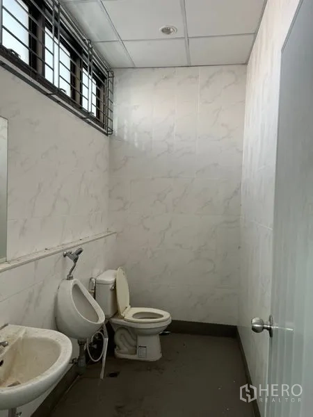 Warehouse for rent in Lat Krabang, Bangkok - Staff restroom with tiled walls, toilet, urinal, sink, and ventilated window.