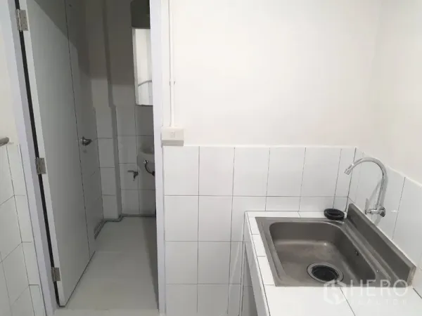 Shophouse for rent in Phra Khanong, Bangkok - Compact pantry with a stainless-steel sink and tiled walls next to a bathroom.