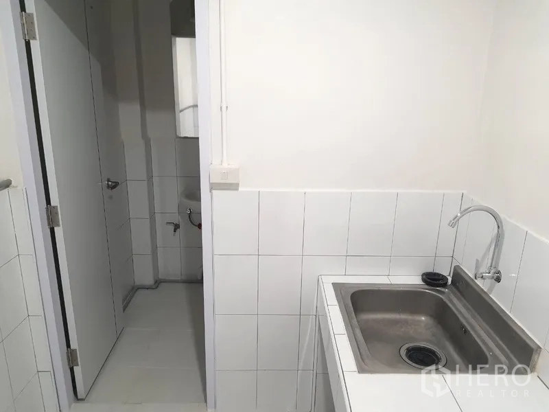 Shophouse for rent in Phra Khanong, Bangkok - Compact pantry with a stainless-steel sink and tiled walls next to a bathroom.