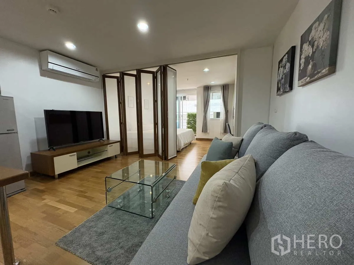 Condominium for rent in Khlong Toei, Bangkok - Living room with TV console and folding doors opening to a light‑filled bedroom.