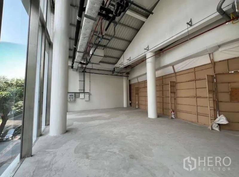 零售空间 出租在Phaya Thai, Bangkok - 纵深开间的高挑零售区，街侧整面玻璃，配有配电箱与临时板墙。