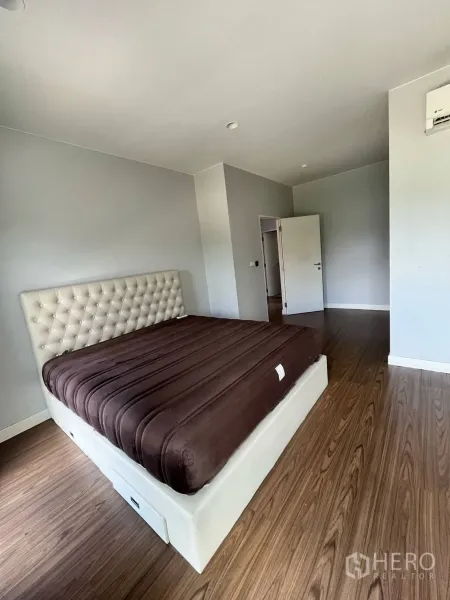 Detached House for rent or sale in Lam Luk Ka, Pathum Thani - Master bedroom with tufted headboard, wood flooring and neutral walls.