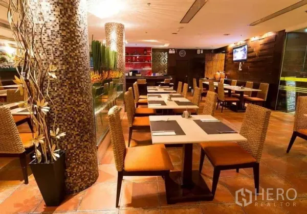 零售空间 出租在Khlong Toei, Bangkok - 暖色灯光的用餐区，马赛克立柱、藤编椅和瓷砖地面。