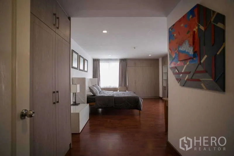 Condominium for rent or sale in Watthana, Bangkok - Spacious bedroom with built-in wardrobes, desk and curtained window.