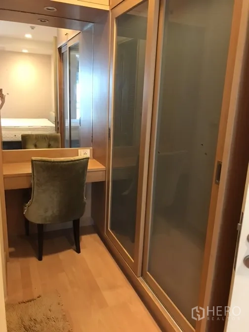 Condominium for rent in Khlong Toei, Bangkok - Walk-in dressing area with built-in vanity, mirror and sliding wardrobes in wood finish.