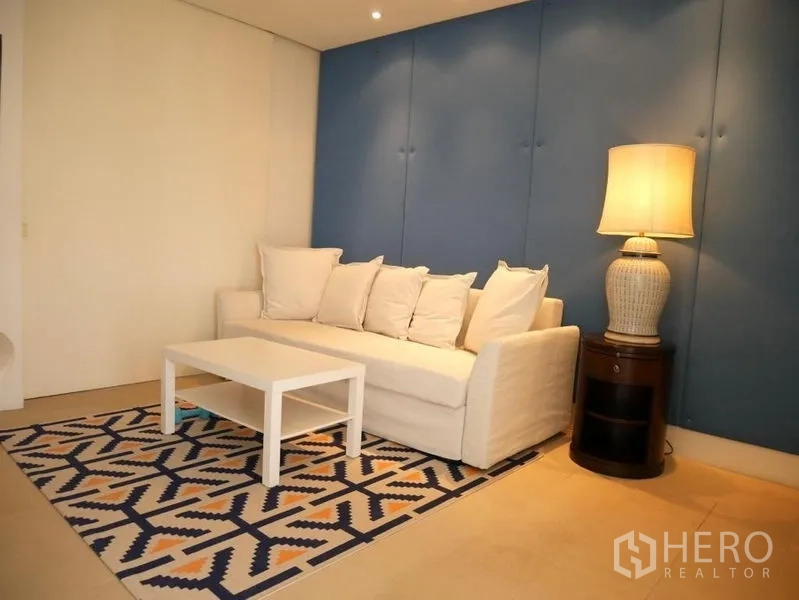 Condominium for rent in Khlong Toei, Bangkok - Cozy lounge room with white sofa, patterned rug and soft lighting.