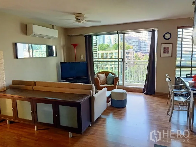 Condominium for rent in Khlong Toei, Bangkok - Open-plan living room with sofa set, TV and sliding doors to a balcony overlooking greenery.
