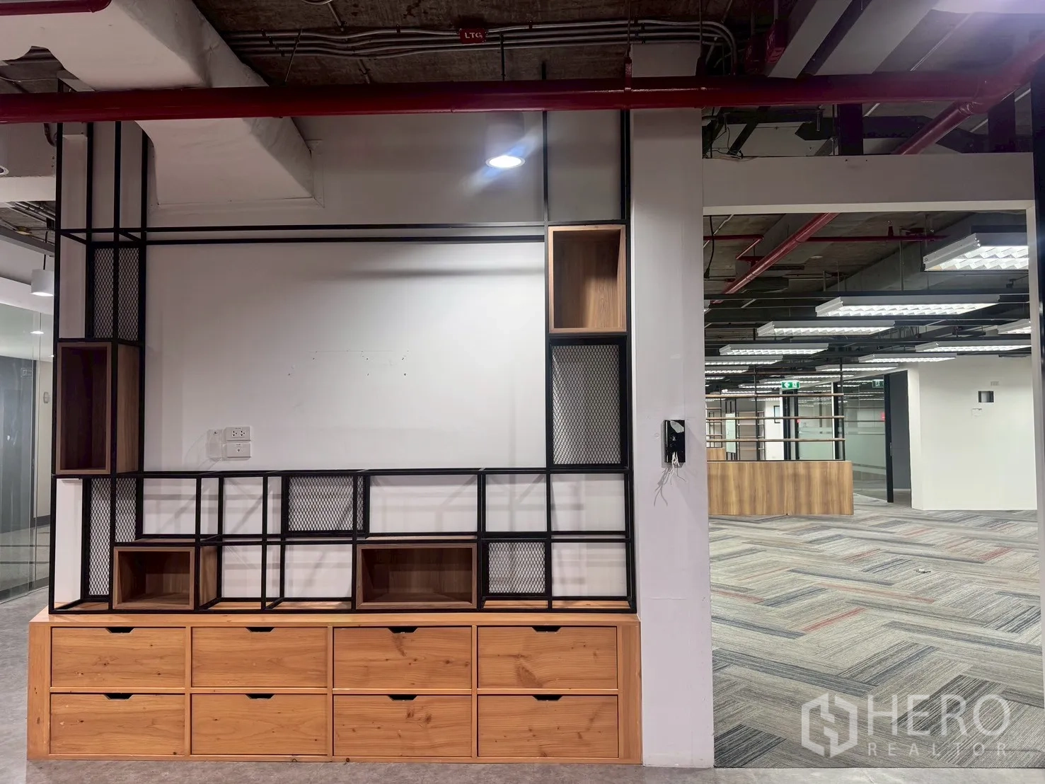 办公室 for rent in Watthana, Bangkok - 内置木质收纳与黑色金属隔架，面向铺地毯与裸露顶的开放式办公区。