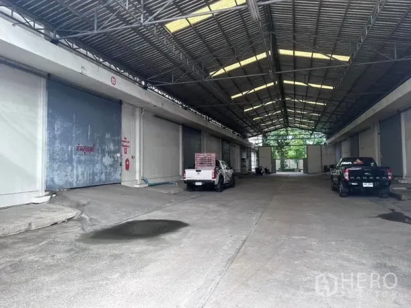 Warehouse for rent in Mueang Samut Prakan, Samut Prakan - Covered drive-through loading bays with multiple large roller shutter doors and parked pickup trucks.