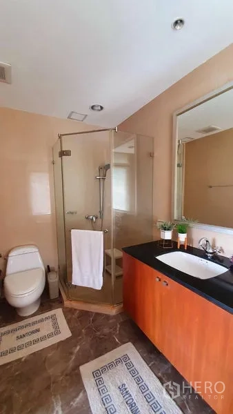 Condominium for rent in Watthana, Bangkok - Bathroom with glass shower enclosure, vanity with black countertop and toilet.