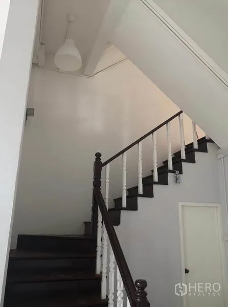 Townhouse for rent or sale in Din Daeng, Bangkok - Interior staircase with dark wooden steps and white balustrade beneath a high ceiling.