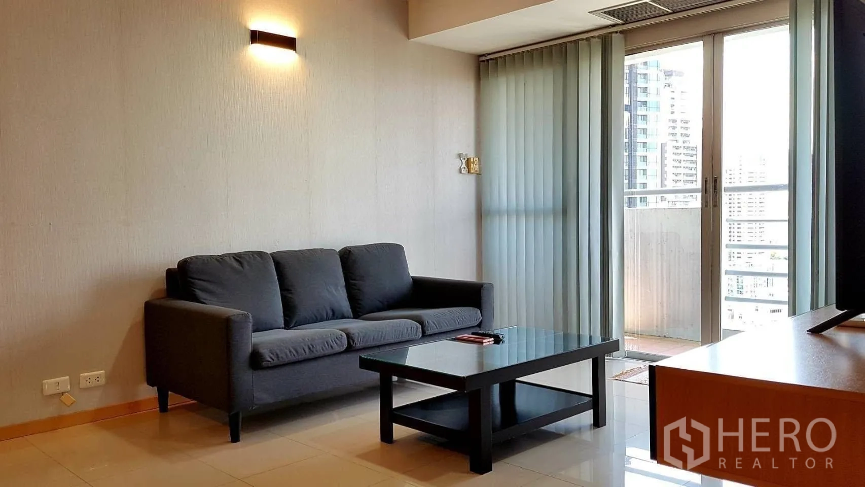 คอนโด for rent in Khlong Toei, Bangkok - ห้องนั่งเล่นสว่างมีโซฟาสีเข้ม โต๊ะกลางกระจก และประตูกระจกออกสู่ระเบียงชมวิวเมือง