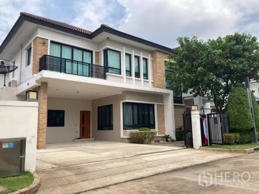 Detached House for rent in Mueang Nonthaburi, Nonthaburi - Two-storey detached house with covered parking, balcony railings and a neatly landscaped front yard.